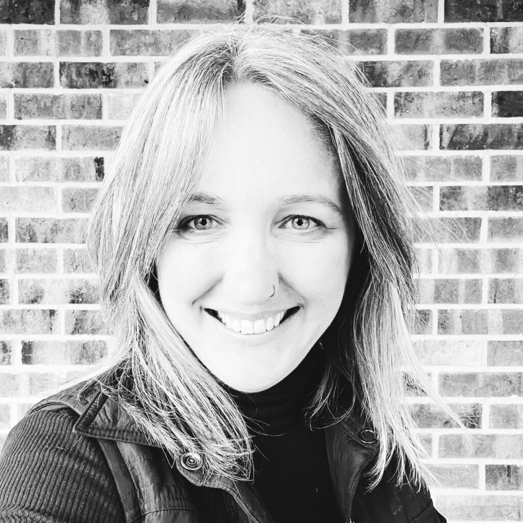Black and white headshot of a woman in front of a brick wall.