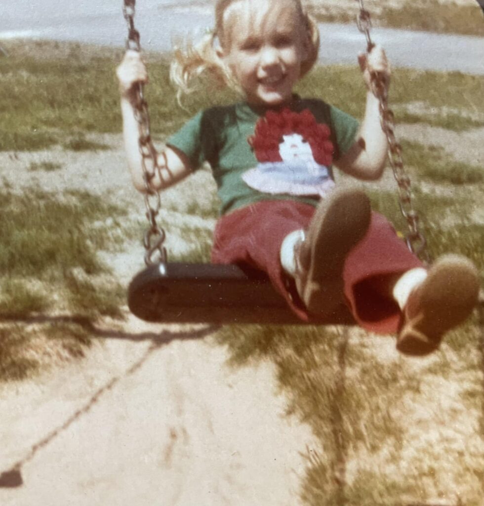 1980s girls with blond pigtails, a Raggedy Ann t-shirt, and maroon corduroys swinging
