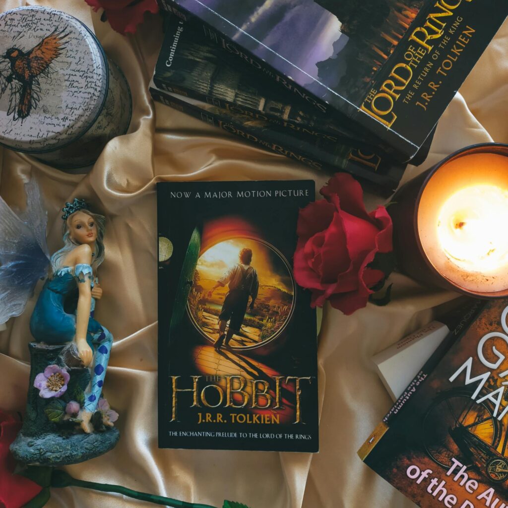 A cozy arrangement featuring fantasy novels, including The Hobbit, glowing candles, and decorative roses.
