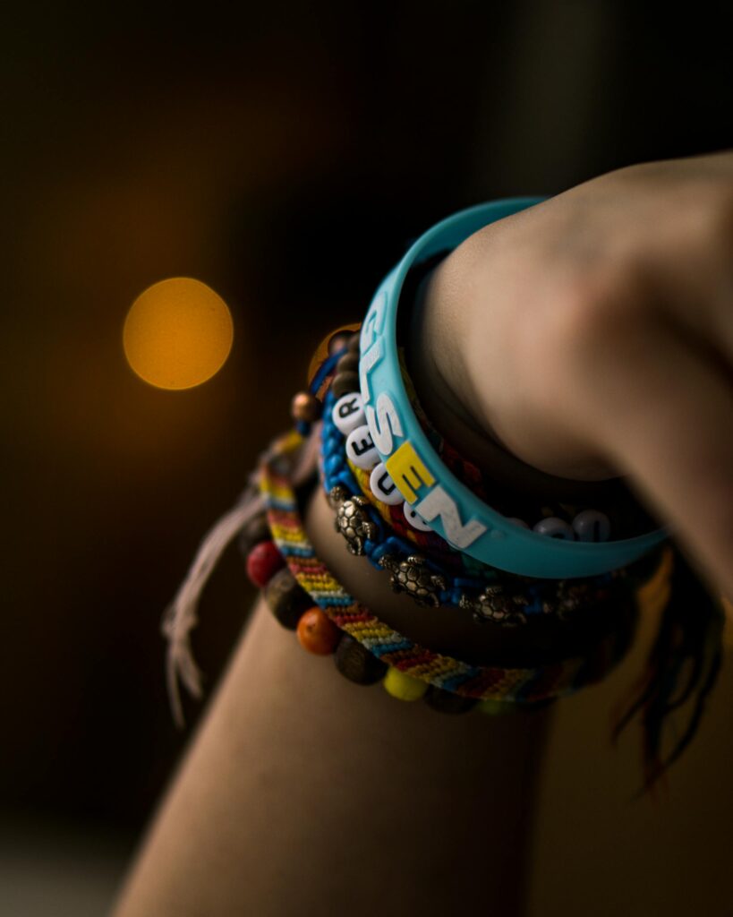 Close-up of a hand wearing colorful bracelets, including a friendship bracelet, emphasizing textures and bokeh effect.
