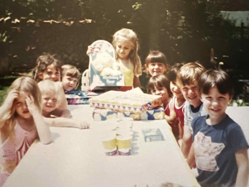 6-year-old girl at her 1983 birthday party holding a yellow Care Bear named Birthday Bear with a cupcake belly badge.
