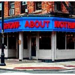 Street-corner diner styled like Tom’s Restaurant with a bright blue sign reading ‘A Show About Nothing,’ referencing the sitcom Seinfeld.