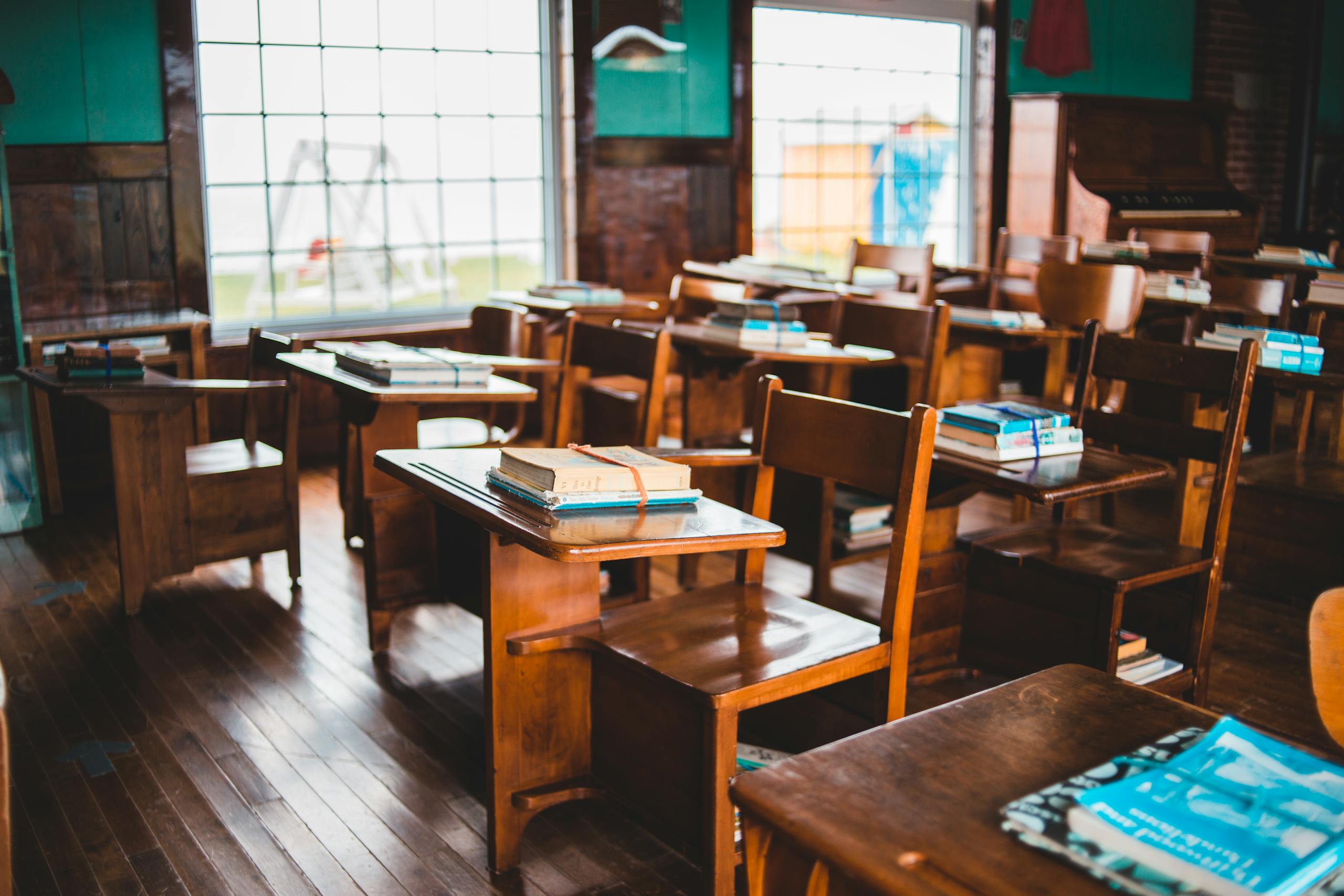 An empty vintage classroom with wooden desks and books on each desk, reflecting a classic educational setup.