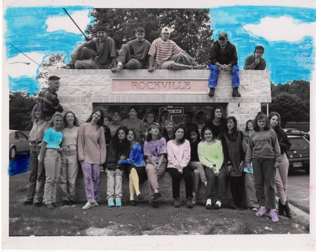 Black-and-white class photo of a high school photography class sitting and standing around a school sign outdoors in 1993.