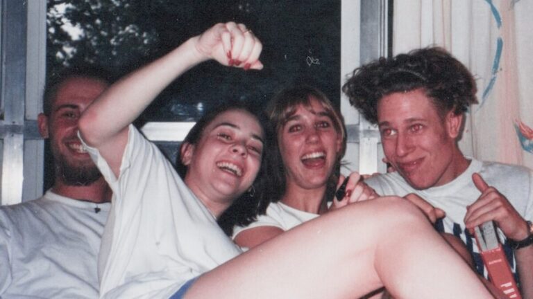 Four friends laughing together on a couch in the 1990s, captured on film before the era of social media documentation.