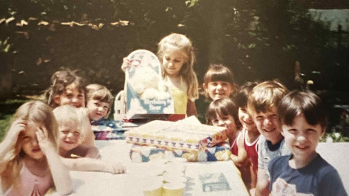 Girl opening a Birthday Bear Care Bear at a 1984 birthday party surrounded by friends