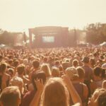 Large crowd at an outdoor 1990s music festival facing a distant stage in warm sunlight