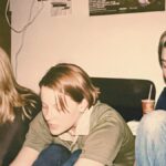 Group of teenage friends hanging out together in the 1990s, music playing in the background